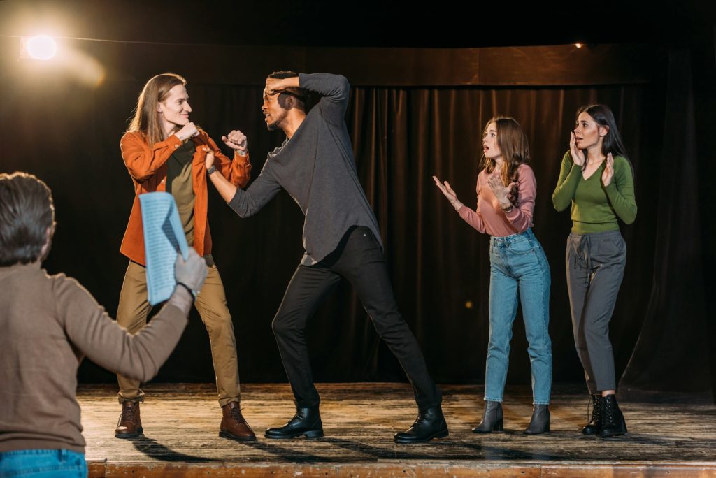 multicultural actors rehearsing fight on stage in theatre