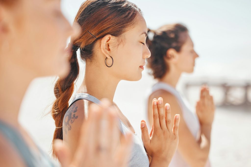 Women friends meditation while training yoga exercise on the beach. Group of zen female athlete wor